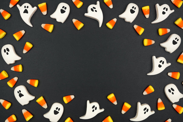 Halloween frame of candy corn and spooky chocolate ghosts. Top view on a black background. Copy space. - Fotoğraf, Görsel
