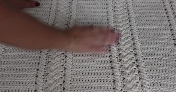 Surface of a crochet blanket with intertwined braids finished in beige cotton yarn, embossed stitch pattern, adult female hands touching it, red nails. Handmade craft creativity - Séquence, vidéo