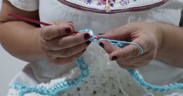 Senior female hands knitting the edge with a stretchy pattern in blue cotton yarn on a white crochet blanket, pink metal hook, original embossed crochet stitch pattern. Handmade craft creativity - Video, Çekim