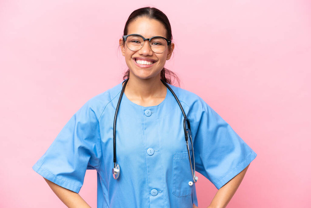 Young nurse Colombian woman isolated on pink background posing with arms at hip and smiling - 写真・画像
