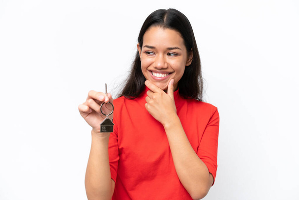 Young Colombian woman holding home keys isolated on white background thinking an idea and looking side - Foto, immagini