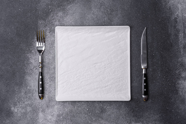 Пустая квадратная белая тарелка поверх серой доски. Вид с воздуха, с местом для копирования - Фото, изображение