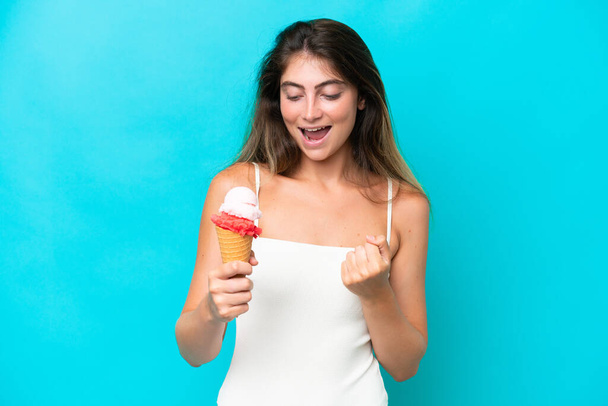 Young woman in swimsuit holding an ice cream isolated on blue background celebrating a victory - Photo, image