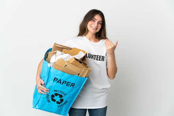 Young woman holding a recycling bag full of paper to recycle isolated on white background inviting to come with hand. Happy that you came - Φωτογραφία, εικόνα