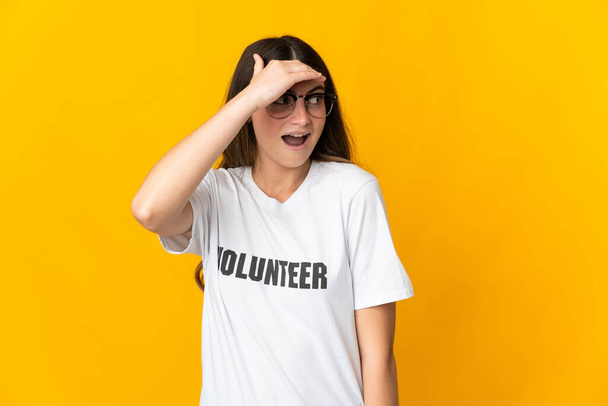 Giovane donna volontaria isolata su sfondo giallo facendo gesto a sorpresa mentre guarda di lato - Foto, immagini