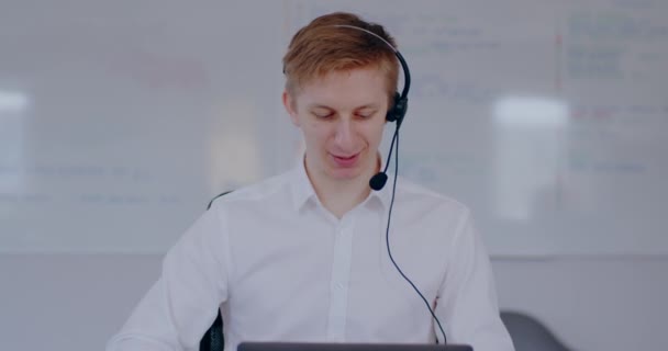 Young man doing video meeting using headset talking. Businessman working online, talking with client. Man working at helpdesk support, remote work, home office. - Materiaali, video