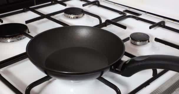 Close-up when olive oil is poured into a pan before starting preparation of a delicious meal, black grates, burners, white cover, black non-stick pan, glass bottle. Concept of delicious homemade food - 映像、動画