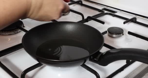 Adult female hands placing two eggs in a pan on a gas stove, fried eggs, full yellow yolk, egg white, oil, fire on, burner, white cover, metal grill. Concept of delicious homemade food - Filmagem, Vídeo