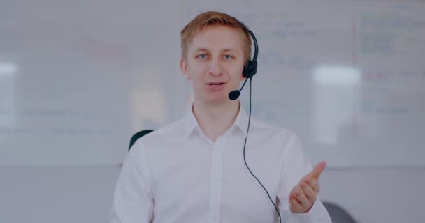 Young man doing video meeting using headset talking. Businessman working online, talking with client. Man working at helpdesk support, remote work, home office. - Materiaali, video