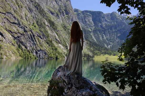 A young woman stands on a stone near a mountain lake of emerald color. High quality photo - Foto, imagen