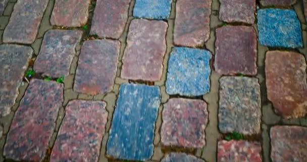 The road is moving. The movement of the road from the pavers. Moving paving stones, top view through the eyes of a person. Pavement from old beautiful multi-colored stones. Sidewalk cigarette butts - Imágenes, Vídeo