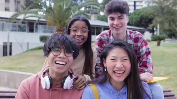 Мультирасовая группа друзей-школьников, сидящих на улице и улыбающихся в камеру - Кадры, видео