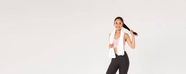 Sport, gym and healthy body concept. Full length of healthy and active, smiling asian fitness girl, brunette female athlete, wiping sweat with towel after good workout, training session in gym. - Φωτογραφία, εικόνα