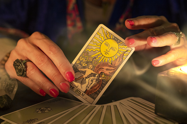 Fortune teller female hands showing The Sun tarot card, symbol of positivity and optimism, during a reading. Close-up with candle light and smoke, moody atmosphere. - Zdjęcie, obraz