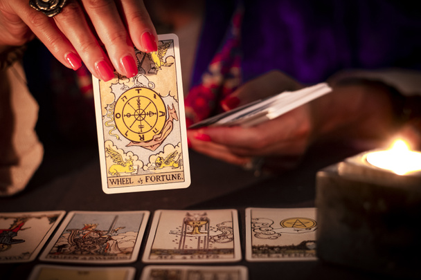 Fortune teller γυναικεία χέρια που δείχνουν το Wheel of Fortune tarot κάρτα, σύμβολο της καλής τύχης, κατά τη διάρκεια της ανάγνωσης. Κοντινό πλάνο με κερί φως, κυκλοθυμική ατμόσφαιρα. - Φωτογραφία, εικόνα