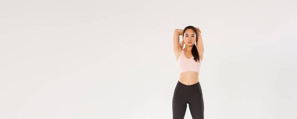 Plná délka soustředěné a motivované asijské atelte, brunetka fitness dívka hledá odhodlaný při provádění strečink cvičení, zahřátí před tréninkem, držení za ruce. - Fotografie, Obrázek