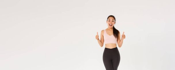 Full length of amazed and satisfied smiling fitness girl, female athelte in active wear liking new gym or workout program, showing thumbs-up pleased, encourage start training or doing exercises. - Photo, Image