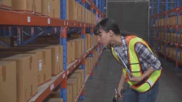 Молодая кавказская работница проверяет со сканирующим штрих-кодом и записывает в буфер обмена для распределения грузов на складе на заводе, транспорте и судоходстве, логистическая концепция. - Кадры, видео