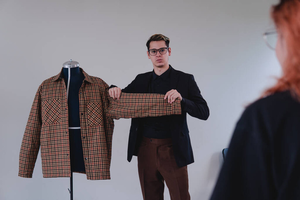 Elegant fashion designer. Caucasian blond man dressed in black shirt, brown pants and glasses working as a tailor. High quality photo - Valokuva, kuva