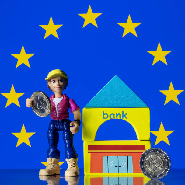 Human figurine, symbolic bank building, euro coins and EU flag - Foto, afbeelding