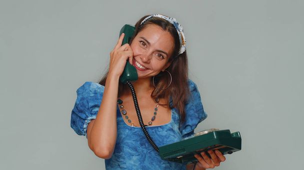 Hey you, call me back. Pretty young woman in princess dress talking on wired vintage telephone of 80s, says hey you call me back. Adult stylish female girl isolated on gray studio background indoor - Fotó, kép