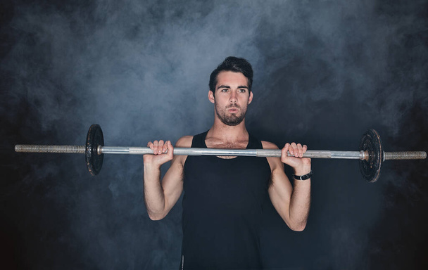It takes discipline and dedication and hes got both. Studio shot of a young man working out with a barbell against a gray background - Zdjęcie, obraz