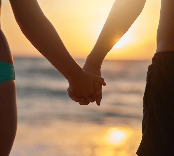 Άλλο ένα ρομαντικό ηλιοβασίλεμα στην παραλία. Κοντινό πλάνο ενός νεαρού ζευγαριού να κρατιέται χέρι-χέρι βλέποντας το ηλιοβασίλεμα στην παραλία - Φωτογραφία, εικόνα