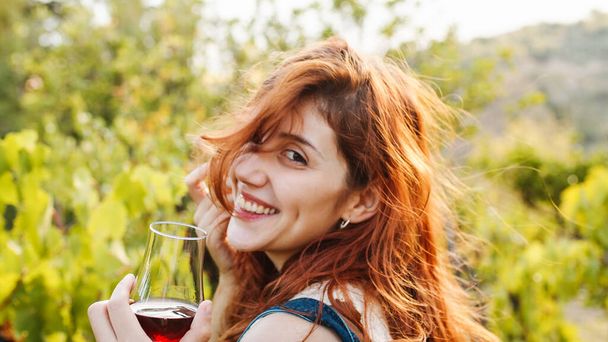 Молодая красивая девушка с кубком красного вина возле виноградников с качественным виноградом - Фото, изображение