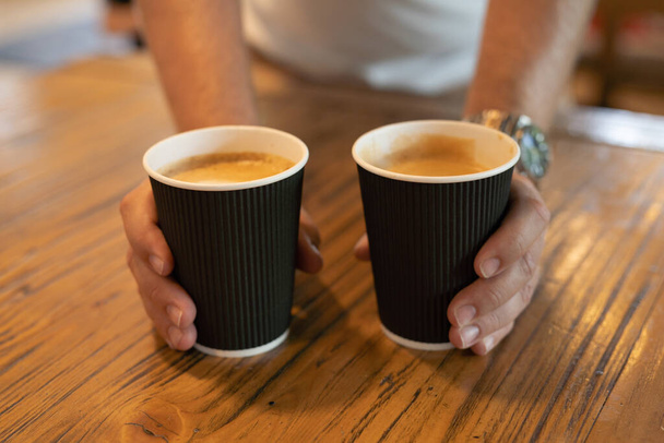 people, drinks and care concept - close up of man hands giving coffee cups in a cafeteria. - Zdjęcie, obraz
