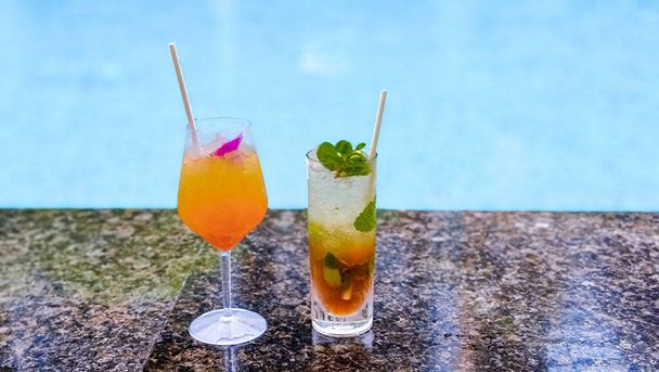 Orange cocktail and mojito at a swimming pool on a luxury vacation, cocktails on the edge of a pool on a vacation holiday concept - 写真・画像