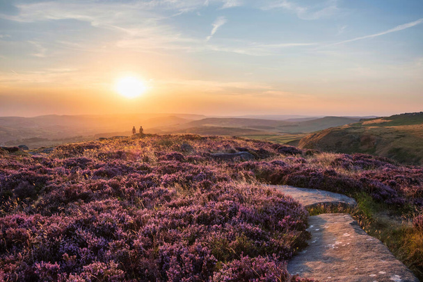 Absolutely stunning sunset landscape image with unidentified couple looking from Higger Tor in Peak District across to Hope Vally in late Summer with heather in full bloom - Fotografie, Obrázek