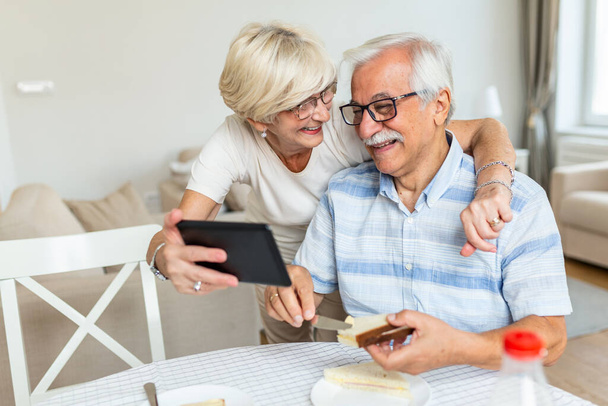 Senior couple taking a selfie with tablet. Elderly couple having a video call with friends or family using tablet. Old couple is talking online via video connection on the tablet. - Fotografie, Obrázek