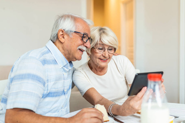 Senior couple smiling and looking at the same tablet hugged. Indoor, at home concept. Mature and retired man and woman using technology - lockdown and quarantine lifestyle - Zdjęcie, obraz