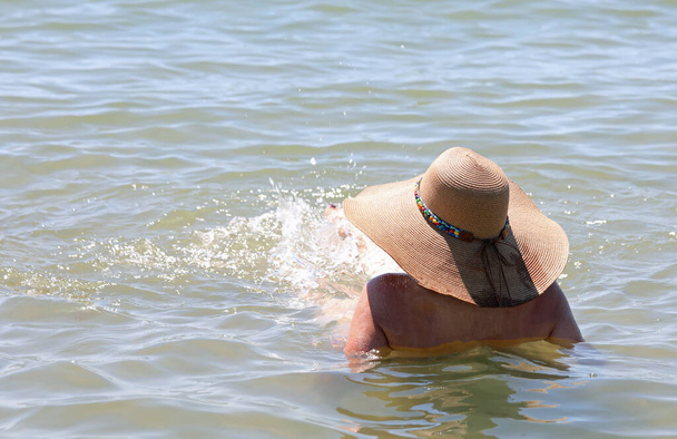 woman relaxing in the middle of the ocean water with a big straw hat to shelter from the sun - Valokuva, kuva