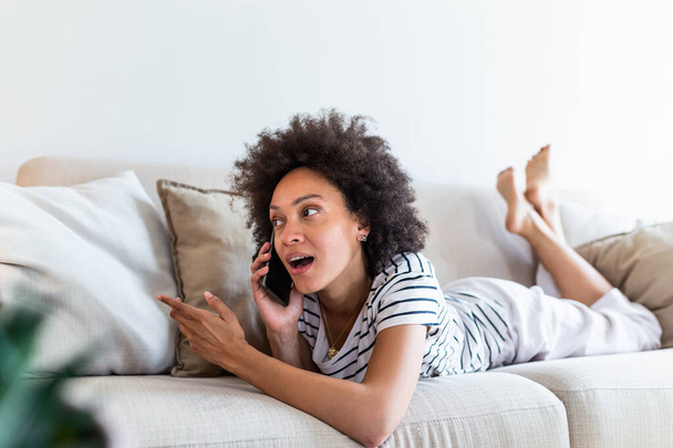 Happy young woman caller talking on her mobile phone at home, cheerful teen girl enjoys pleasant mobile conversation, smiling millennial female holding cell phone making call in living room - Foto, Imagem
