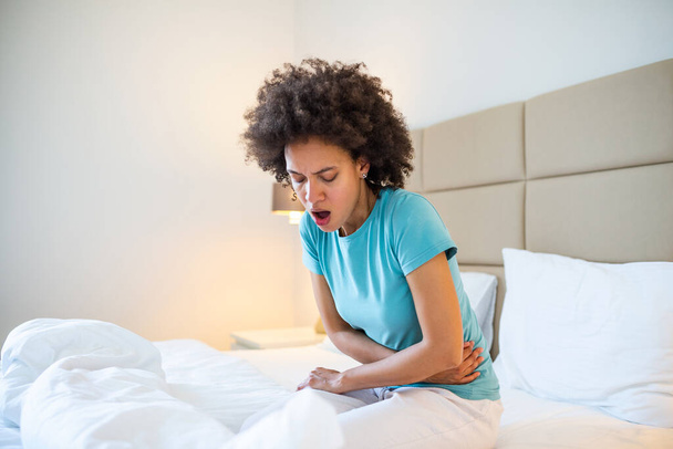 Vrouw in pijnlijke uitdrukking houdt handen tegen buik lijden menstruele periode pijn, ligt verdrietig op bed, met buikkramp in vrouwelijke gezondheid concept - Foto, afbeelding