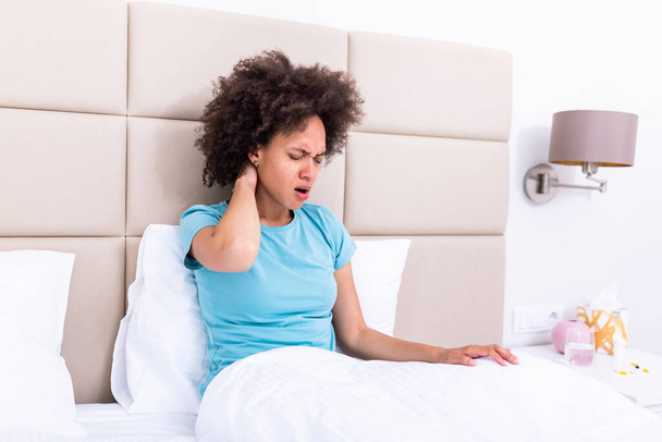 Young woman sitting on the bed with pain in neck touches her neck suffers from painful feelings ache caused by poor wrong posture, sedentary work, sitting for long period concept image - Foto, Bild