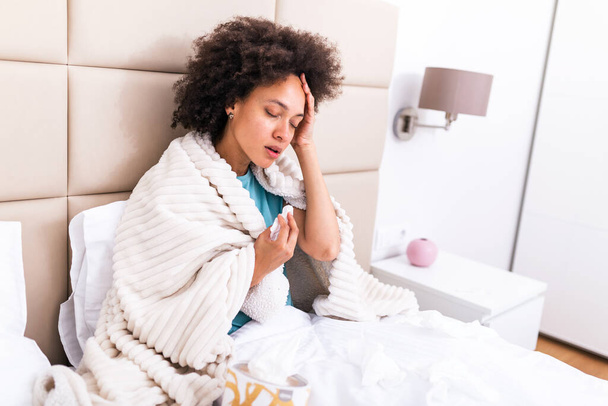 Ill african young woman covered with blanket blowing running nose got fever caught cold sneezing in tissue sit on sofa, sick allergic black girl having allergy symptoms coughing at home, flu concept - Photo, Image