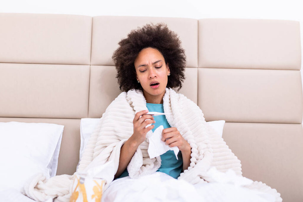 Sickness, seasonal virus problem concept. Woman being sick having flu lying on bed looking at temperature on thermometer. Sick woman lying in bed with high fever. Cold flu coronavirus, covid19 - Photo, Image