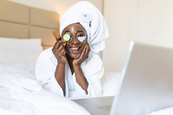 Beautiful young woman with eye mask on her face holding slices of fresh cucumber. Skin care and treatment, spa, natural beauty and cosmetology concept - Foto, imagen