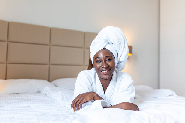 Positive start to the day . Smiling african young woman lying on bed in bathrobe. African american woman relaxing on the bed after bath and looking at the camera - Zdjęcie, obraz