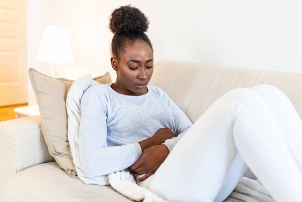 Woman lying on sofa looking sick in the living room. Beautiful young woman lying on bed and holding hands on her stomach. Woman having painful stomachache on bed, Menstrual period - Fotó, kép