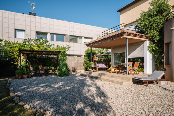 Spacious yard of residential house with veranda equipped with furniture including table chairs and patio swing on sunny day in suburb area - Fotoğraf, Görsel