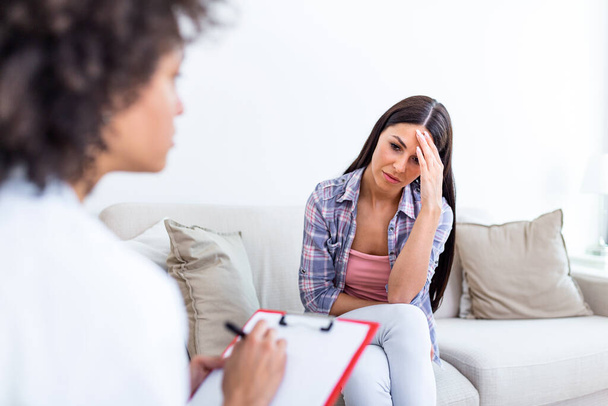 Молода жінка сидить на дивані, покриваючи обличчя руками, відчуває безнадійне, пригнічене або плаче, відвідує психотерапевта, виявляє поганий діагноз або результати медичних тестів
 - Фото, зображення