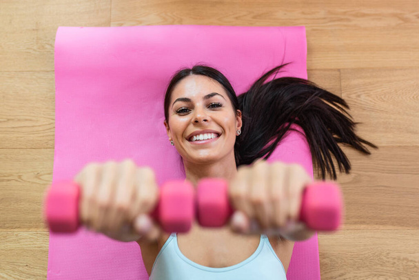 Determined woman losing weight at home and exercising with dumbbells. Sporty pretty woman exercising at home with dumbbells. Fitness, workout, healthy living and diet concept. - Fotoğraf, Görsel