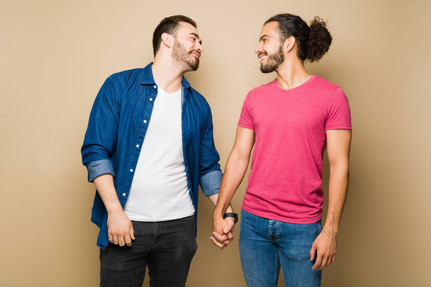 Adorable gay man in love holding hands with his happy boyfriend and flirting during a romantic date - 写真・画像