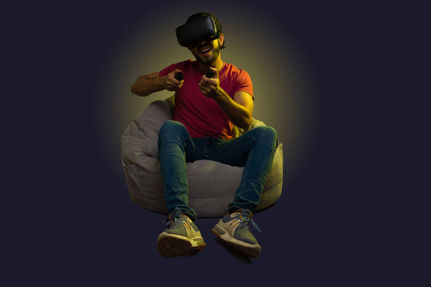 Веселий молодий чоловік грає у веселі відеоігри з окулярами віртуальної реальності, сидячи на бобовій сумці
  - Фото, зображення