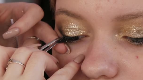 Beautiful bright professional makeup in a beauty studio. Make-up artist glues artificial long eyelashes to give expressiveness to the eyes, close-up view. - Video