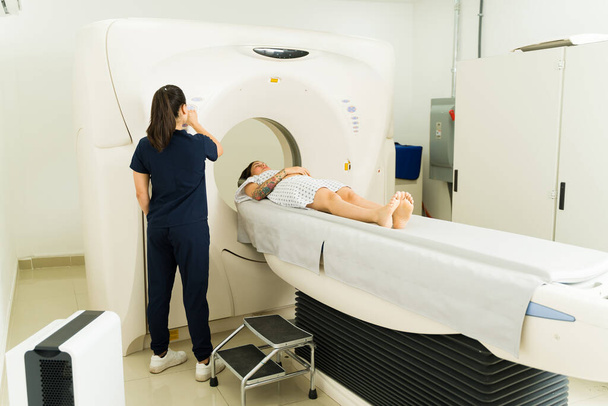 Rear view of a radiologist turning on the x-ray machine machine with a young woman patient doing a tomography of her brain to detect cancer - Foto, Imagen