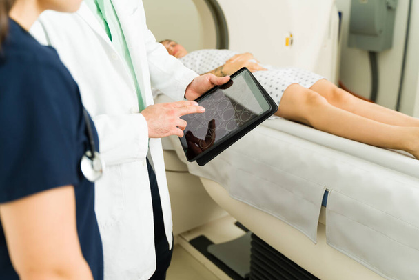 Νοσοκόμα και γιατρός που εξετάζουν τα ιατρικά αποτελέσματα στο δισκίο μιας γυναίκας ασθενούς που κάνει μια αξονική τομογραφία για να ελέγξει για καρκίνο  - Φωτογραφία, εικόνα